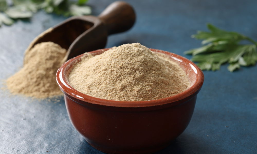 Ashwagandha root powder in a bowl with a wooden scoop and green leaves