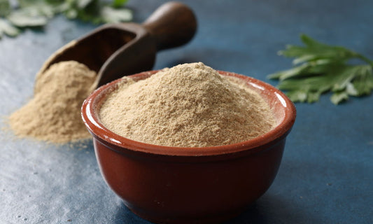 Ashwagandha root powder in a bowl with a wooden scoop and green leaves